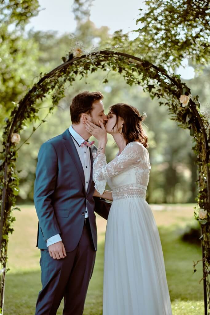 Le baiser des mariés sous l'arche de verdure